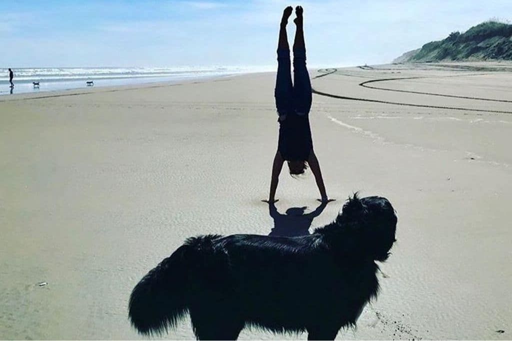 Julie doing a handstand on the beach with dog