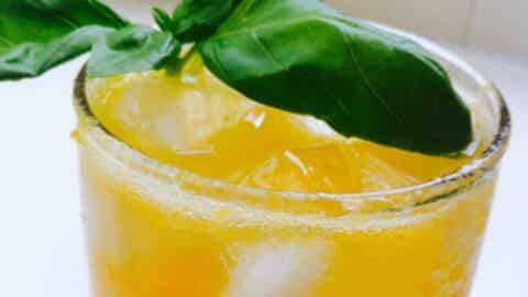 ginger basil drink in a glass with ice and basil leaves