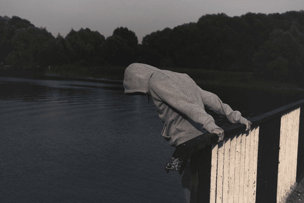 Man leaning over a bridge head facing down